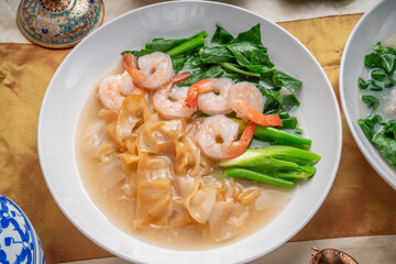Wide Rice Noodles with Shrimp and kale in Gravy Sauce  Served with condiments, chili powder , chili sauce and sugar. Asian food.