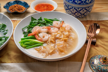Wide Rice Noodles with Shrimp and kale in Gravy Sauce  Served with condiments, chili powder , chili sauce and sugar. Asian food.