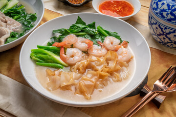 Wide Rice Noodles with Shrimp and kale in Gravy Sauce  Served with condiments, chili powder , chili sauce and sugar. Asian food.