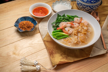 Wide Rice Noodles with Shrimp and kale in Gravy Sauce  Served with condiments, chili powder , chili sauce and sugar. Asian food.