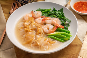 Wide Rice Noodles with Shrimp and kale in Gravy Sauce  Served with condiments, chili powder , chili sauce and sugar. Asian food.