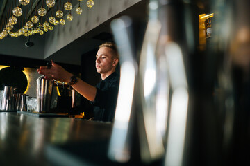 Side low-angle view of confident barman making refreshing alcoholic cocktail standing behind bar...