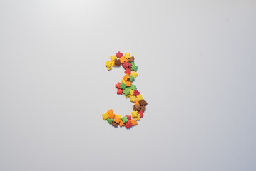 Numeral three from sweet pastry topping in the form of colorful foliage on a white background.