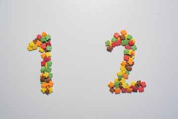 Numeral twelve from sweet pastry topping in the form of colorful foliage on a white background.