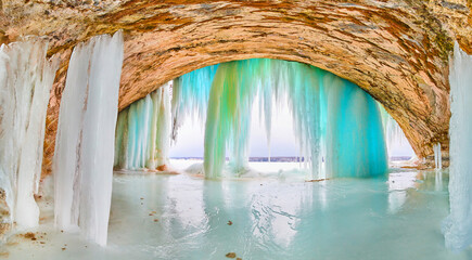 Giant ice cave with tall icicles of blue and green at entrance on lake