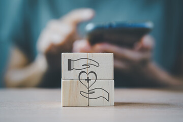 heart icon between hands on wooden cube blocks with blurred senior woman hold smartphone for online...
