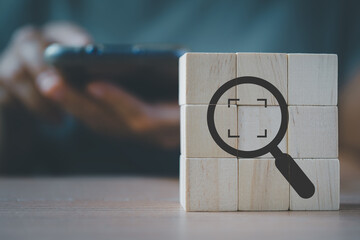 wooden cube blocks with magnifying glass and cropped object symbols with blurred senior holding smartphone for Identify and clarify concept, market and customer target and focusing