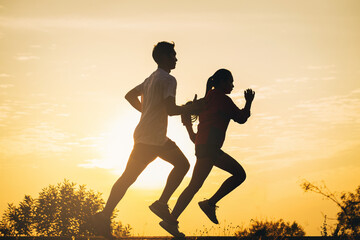 Silhouette of young couple running together on road. Couple, fit runners fitness runners during outdoor workout with sunset background.