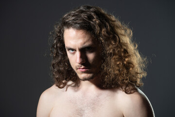 Portrait of sexy handsome guy with curly hair. Macho brutal guy with long curly isolated on gray background.