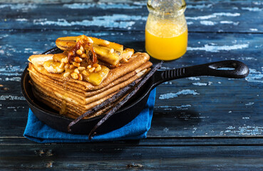 Pancakes caramelized with bananas, honey and nuts in a cast-iron frying pan. Thin pancakes or crepes