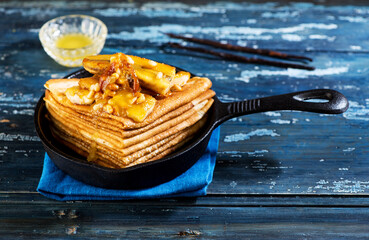 Pancakes caramelized with bananas, honey and nuts in a cast-iron frying pan. Thin pancakes or crepes