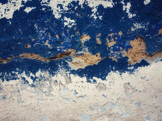 surface of the old cement wall, painted white and blue, has cracks.