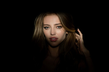 Fototapeta premium Beauty close up face of beautiful pretty girl on black. Woman in shadow. Female model with shadows on face looking seductive and sensual on dramatic black studio with light.