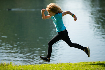 Child boy running or jogging near lake on grass in park. Sporty boy runner running in summer park. Active kids, sport children. Jogging helps the body to be strong.