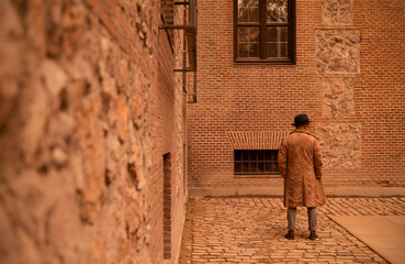 Fototapeta premium Rear view of man in coat standing in front of old building on street during sand storm day. Madrid, Spain