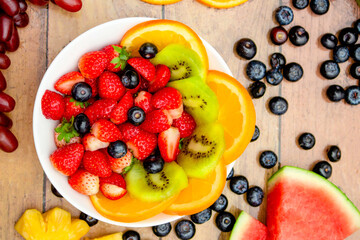 Fresh fruits concept, Tropical fruits and assorted berry salad in bowl on wooden background