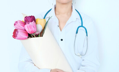Doctor woman of Asian appearance, in white medical clothes with a stethoscope around her neck, holds a bouquet of flowers red tulips in her hands. The concept of congratulations on the day of the medi