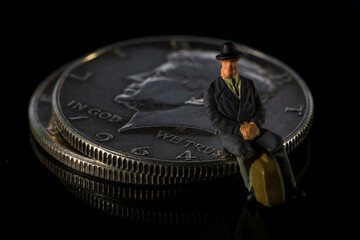 Miniature man seating on Half Dollar coin Black background Macro