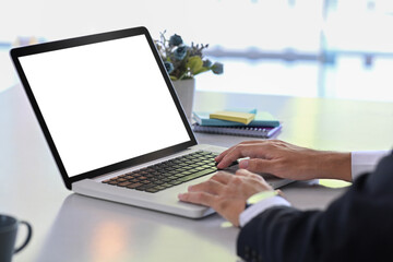Cropped shot businessman sitting at office desk searching information on laptop computer.