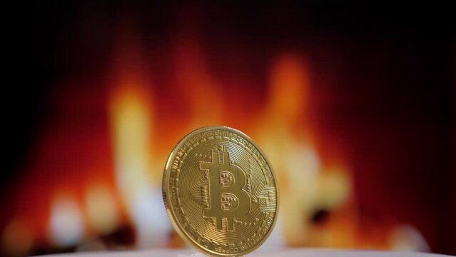 Close-up of a gold bitcoin coin slowly spinning against the background of a burning fire in the fireplace. Digital money, banking, investment, finance and business concept.