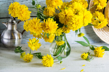 Bouquet of yellow flowers in glass vase on wooden background, still life with yellow summer flowers, pears and straw hat in background