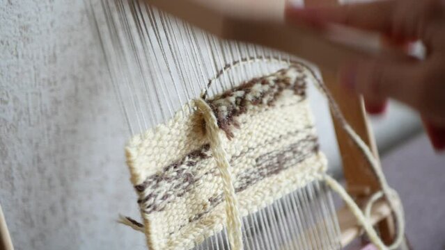 Artisan uses a tapestry beater to push weft threads down. Making mini tapestry piece with hand loom and weft beater