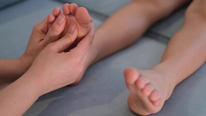 Obraz na płótnie Canvas Mother is doing massage on her baby foot. Prevention of flat feet, development, muscle tone, dysplasia. Capable trained rheumatologist treating patients feet. Masseur massaging children's foot.