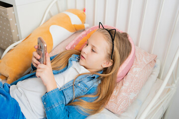a pretty little girl in a rim with cat ears with a phone in bed. 