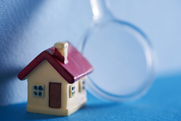 small model house with magnifying glass against blue backgroun