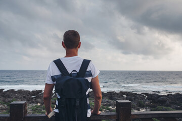 Fototapeta premium Young man standing by the shore looking at the sea and the sky.