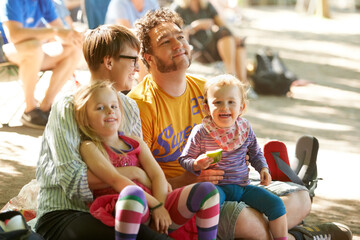 Sitting down to watch the bands. A young family of four sitting down to enjoy the bands at an outdoors music festival. - obrazy, fototapety, plakaty