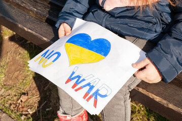 a child with small hands holds a poster no war between Ukraine and Russia drawn by a child on a...
