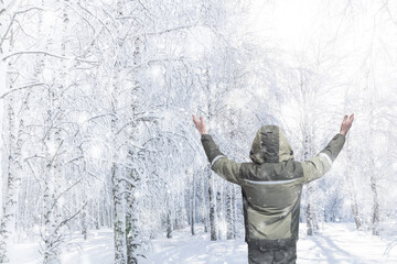 Winter frosty landscape. Man in warm clothes rejoices in nature, raising his hands up. Snowfall. Birch trees are covered with frost and snow on the background of the bright sun.