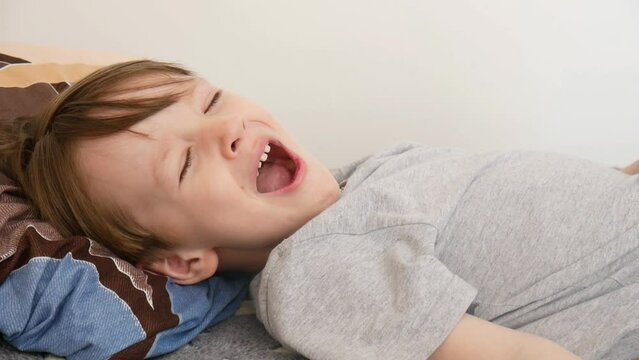 A pretty boy yawns wide falling asleep on the bed