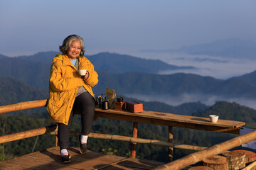 asian senior female retirement age siting at view point relax with coffee making breakfast in beautiful nature and sea,mist in valley winter season