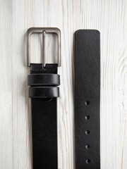 Black fashionable men's leather belt with metal buckle on white wood background. Male accessory. Front top view, vertical photo.