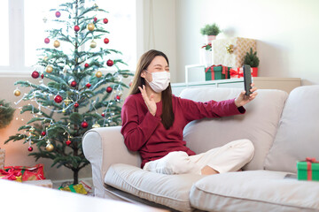 Young Asian woman wear face mask and video call to friend during Christmas holiday season.