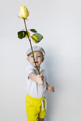 A little boy in retro style with a yellow rose in his hand stands near a white wall.