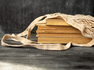 Fototapeta na wymiar Stack of old books on a wooden background. Reusable eco-friendly mesh bag