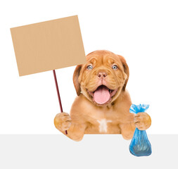 Mastiff puppy holds plastic bag and empty placard above empty white banner. Concept cleaning up dog droppings or eco concept. Isolated on white background