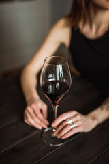 A close-up of a glass of red wine in the hands of a caucasian young woman, sitting at the wooden table