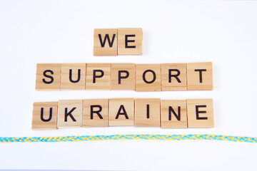 phrase we support ukraine is laid out of wooden squares isolated on white background. with flag of ukraine with blue and yellow ribbon. Concept of peace, war in Ukraine