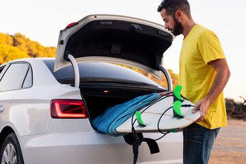 man taking a surfboard out of the trunk of the car