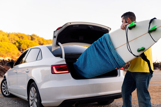 man taking a surfboard out of the trunk of the car