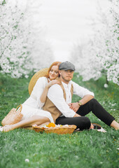 Picnic - Young couple in spring meadow. Alley of flowering cherry trees.