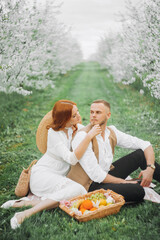 Picnic - Young couple in spring meadow. Alley of flowering cherry trees.