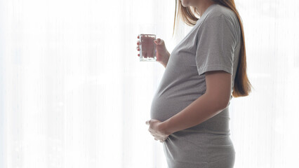 Young pregnant woman drinking water at home, healthcare and pregnancy care concept