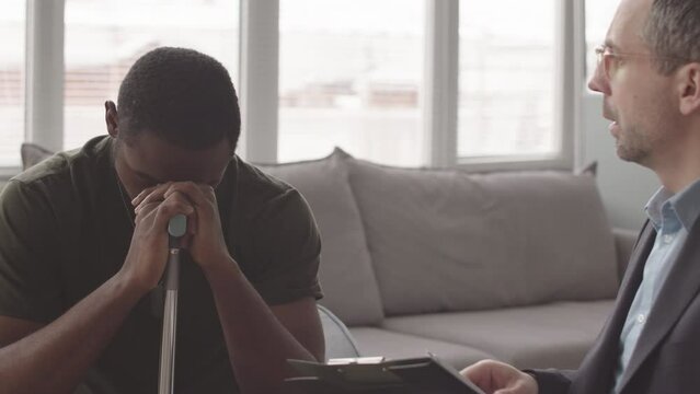 Waist up slowmo of professional military psychologist supporting African American veteran soldier with depression and PTSD, having individual therapy session in modern office