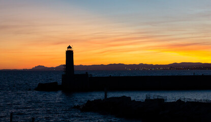Sunset landscape that capture the sea, lighthouse and mountains silhouettes from the city of Nice, France.