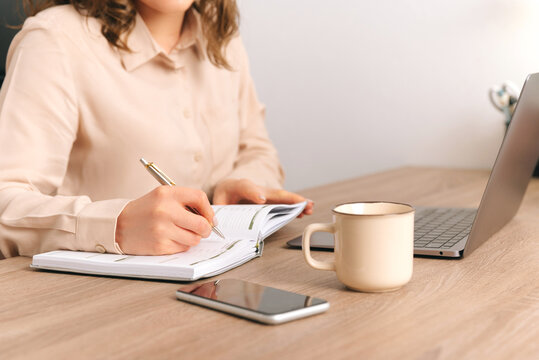 No Face Photo Of A Woman Writing In Her Journal At Work Near Laptop And Phone.